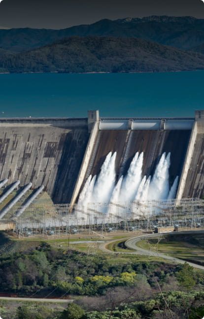 Hydroelectric dam with water flowing over spillways beside a reservoir
