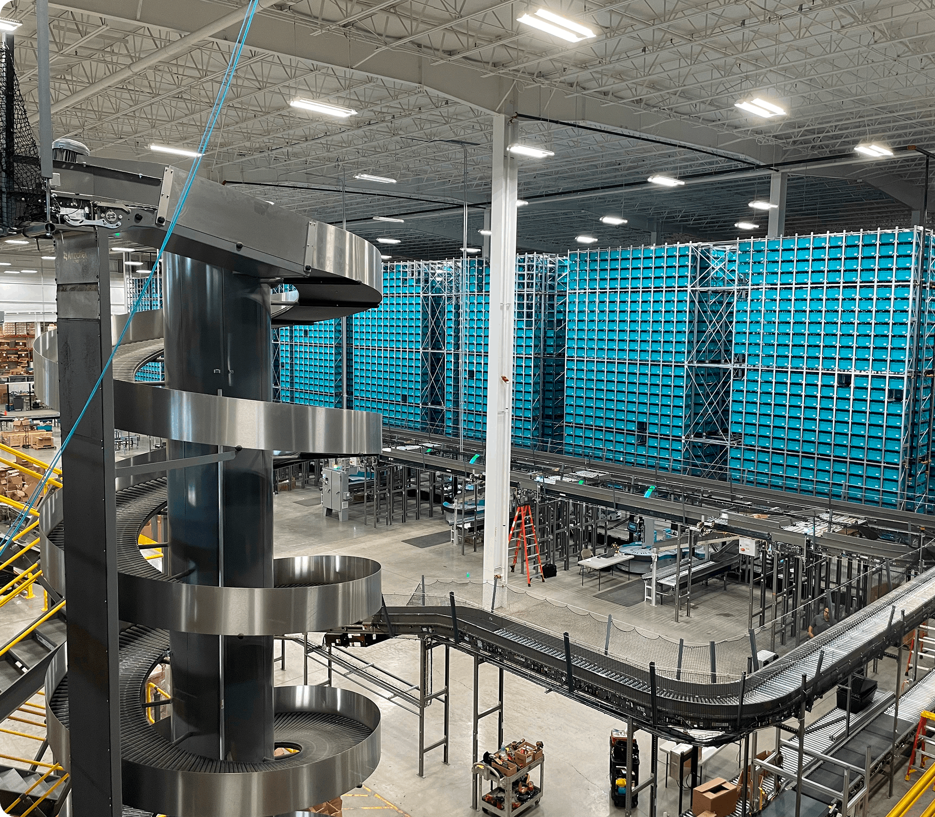Spiral metal chute and conveyor system inside large warehouse with tall blue storage racks and industrial lighting
