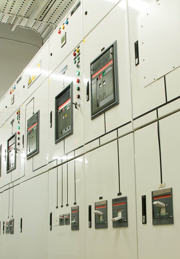 Indoor electrical switchgear with multiple circuit breakers, control handles, indicator lights and labeled metal panels