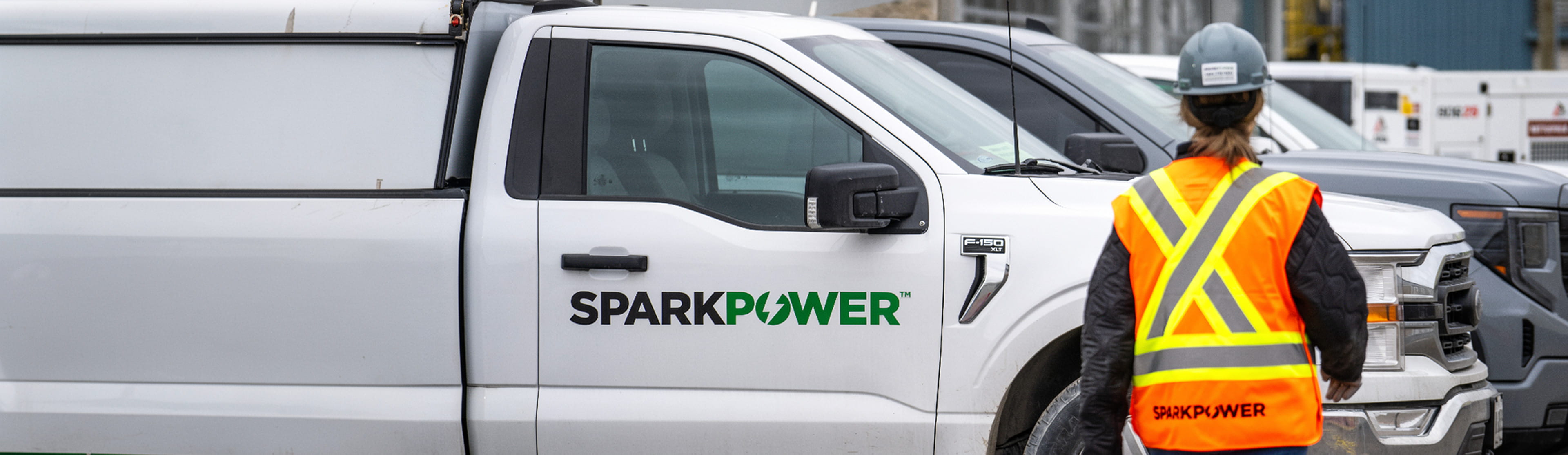 SparkPower service pickup truck beside work trucks with a worker wearing a high-visibility vest and hard hat