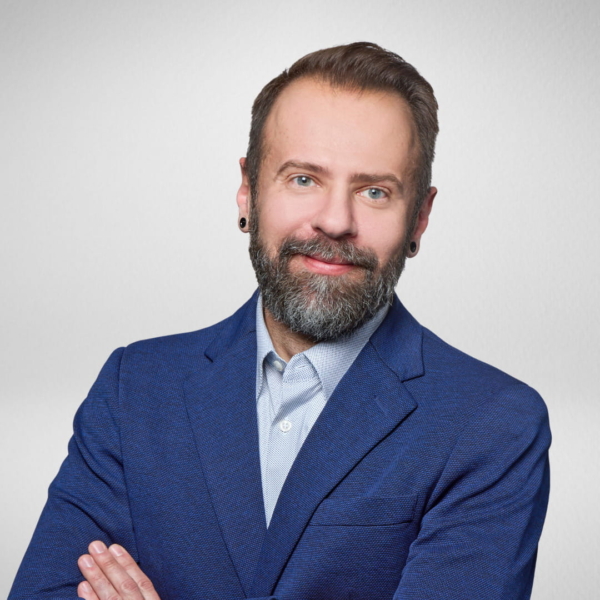 Man in a navy blazer with a gray beard, smiling, arms crossed