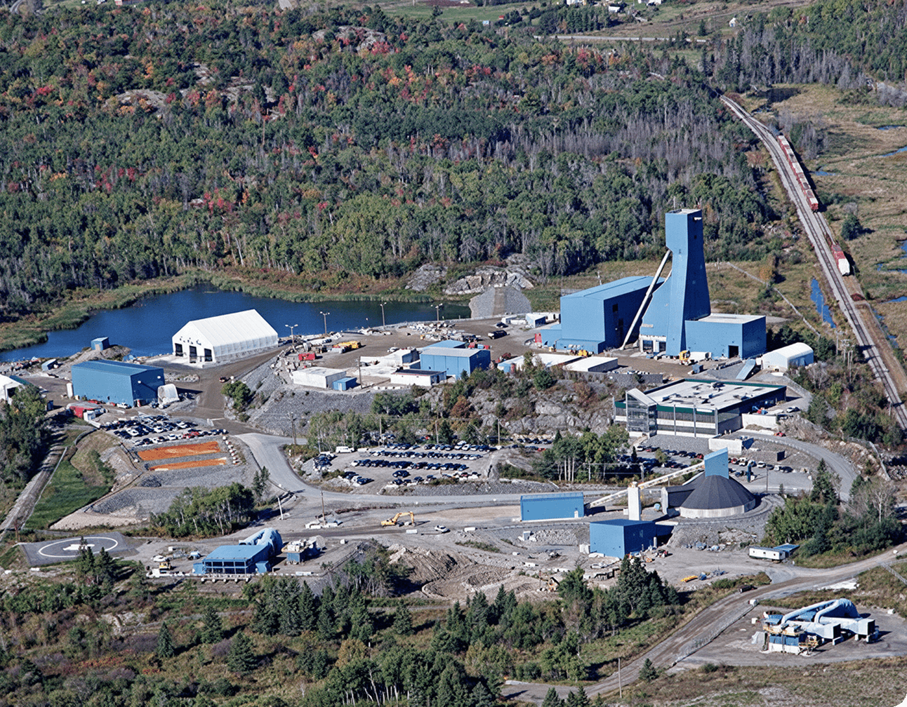 Aerial shot of a mining facility showing blue plant buildings, tall conveyor tower, parking lots, rail spur and pond