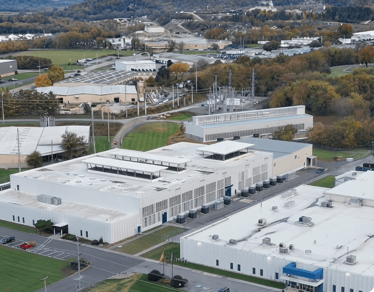 Aerial view of a white industrial data center and adjacent buildings with rooftop cooling units, substations and access roads