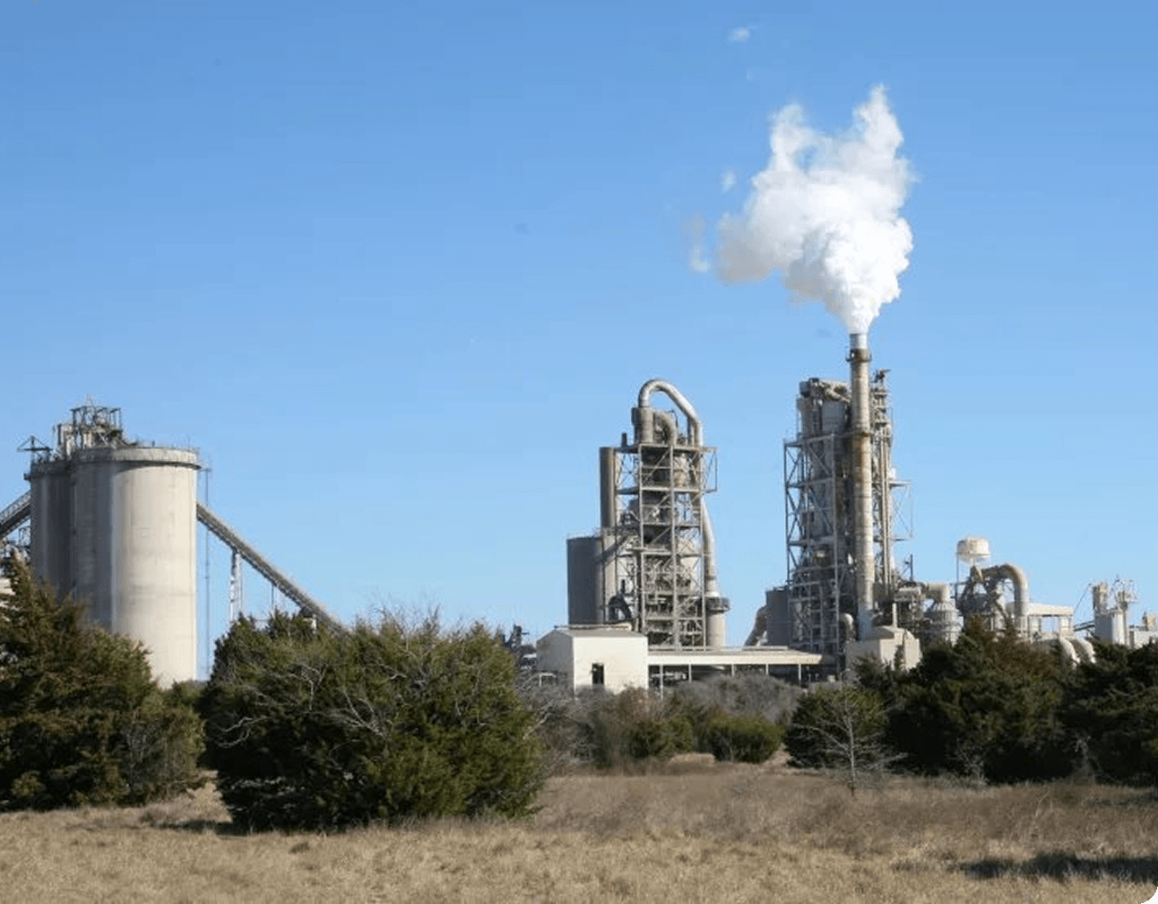 Industrial aggregates plant with silos, processing towers and a smokestack emitting white steam against a clear blue sky