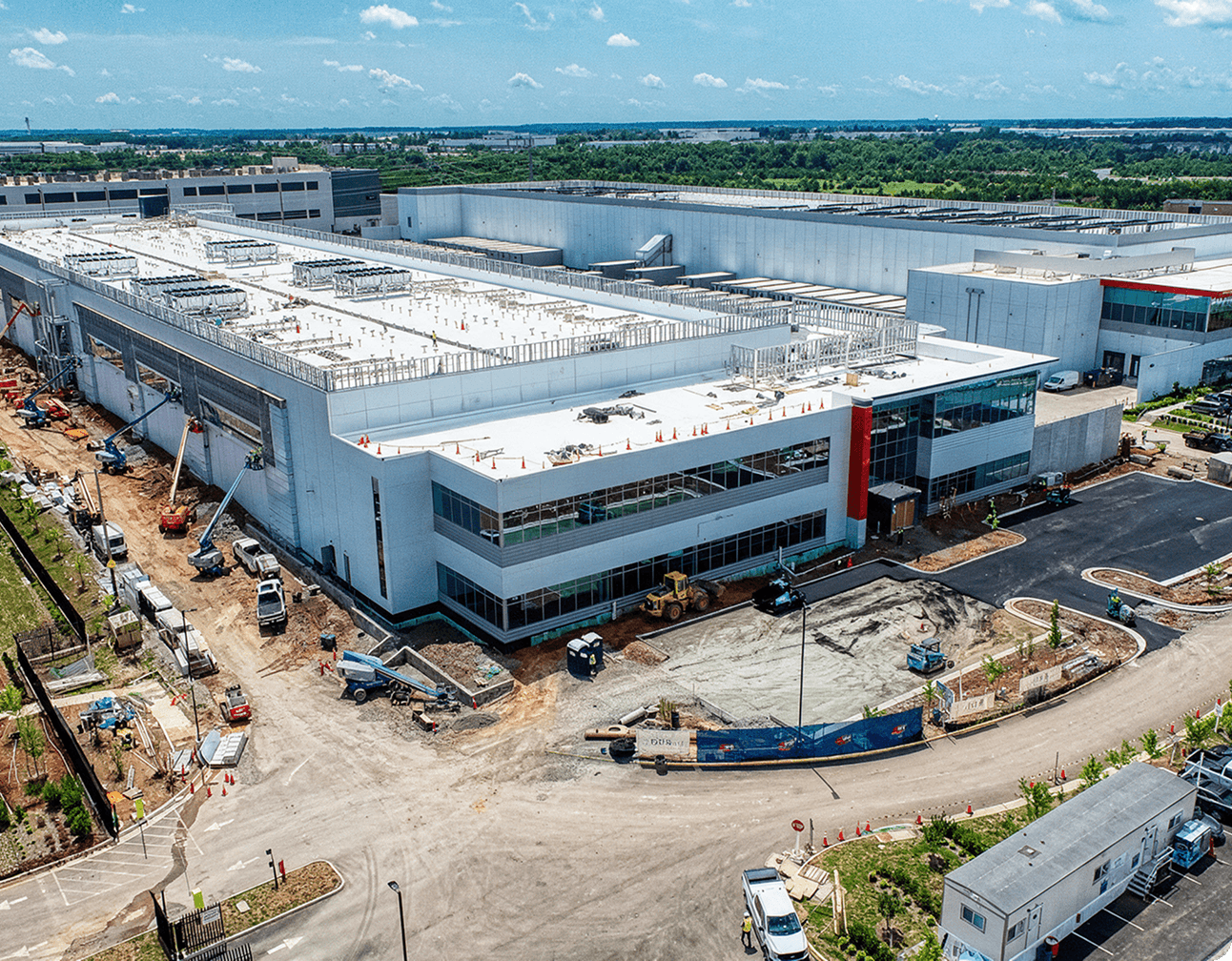Aerial view of a data center under construction with rooftop HVAC units, exterior switchgear areas and construction vehicles