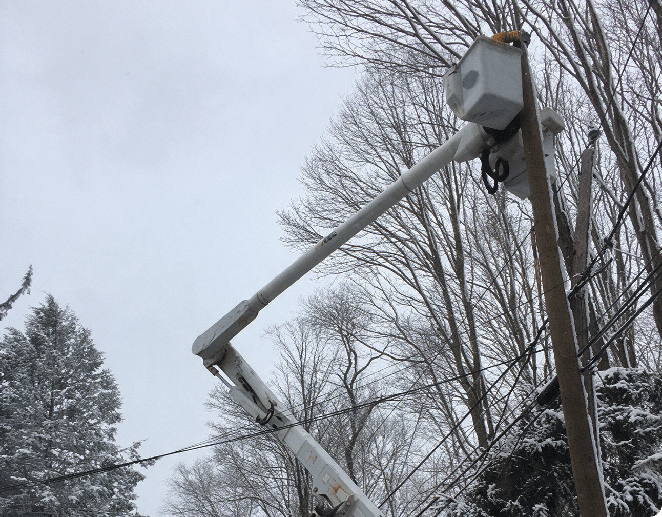 Boom truck bucket servicing snow-covered overhead distribution lines on a wooden pole during storm restoration response