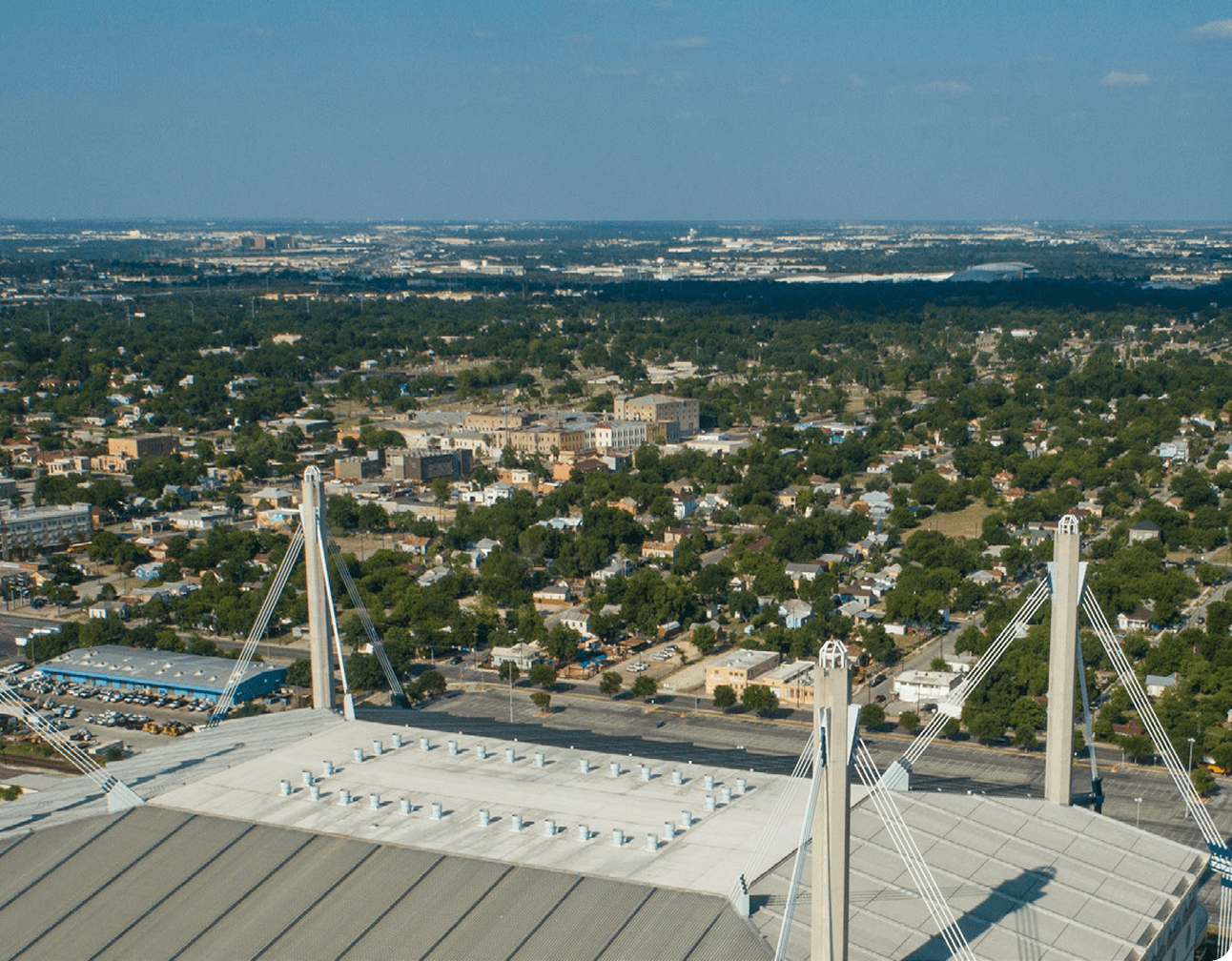 Aerial view of Alamodome roof and cable-stayed support towers with surrounding San Antonio neighborhoods and skyline