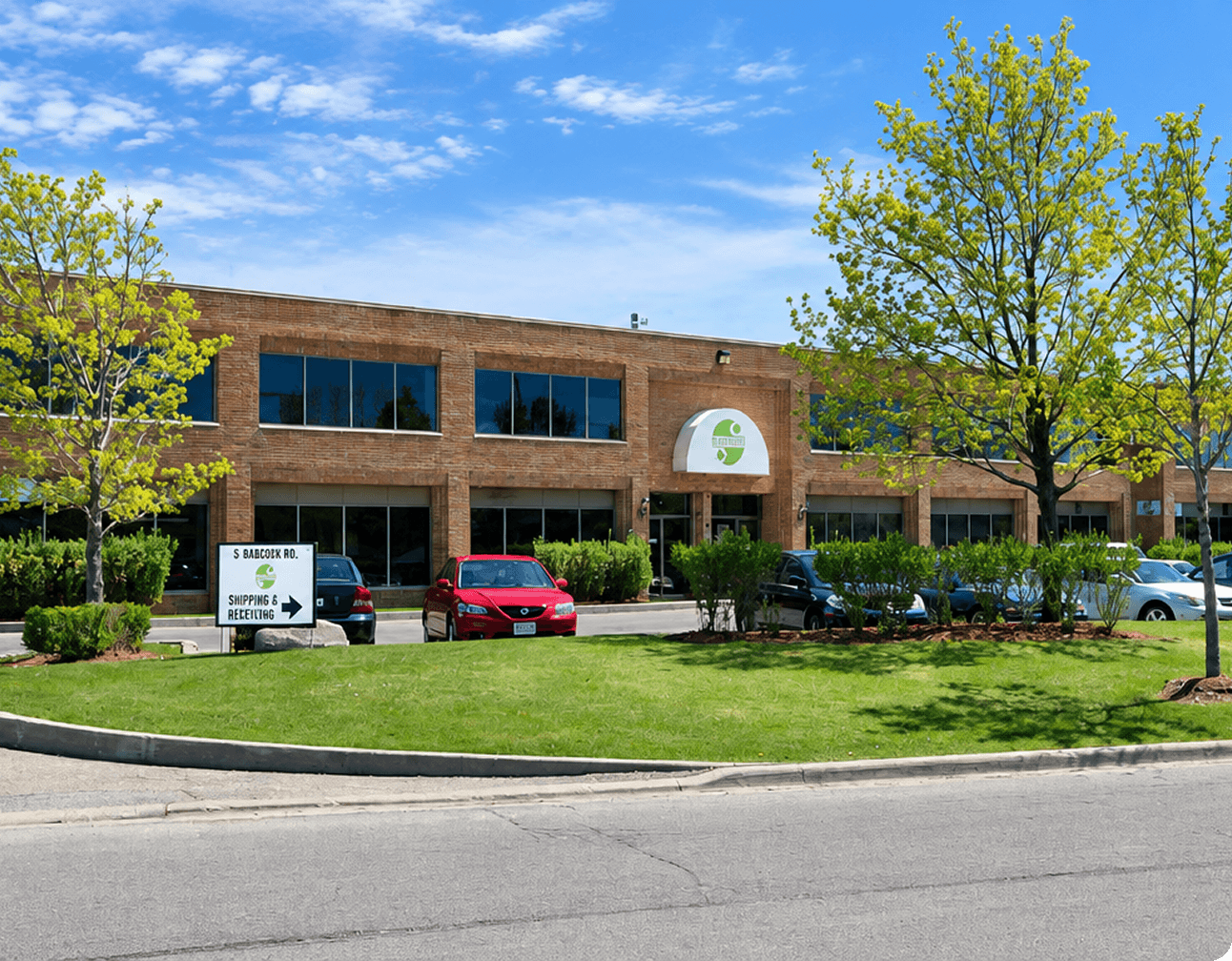 Two-story brick commercial building with company awning, parked cars and landscaped lawn under a blue sky, front view