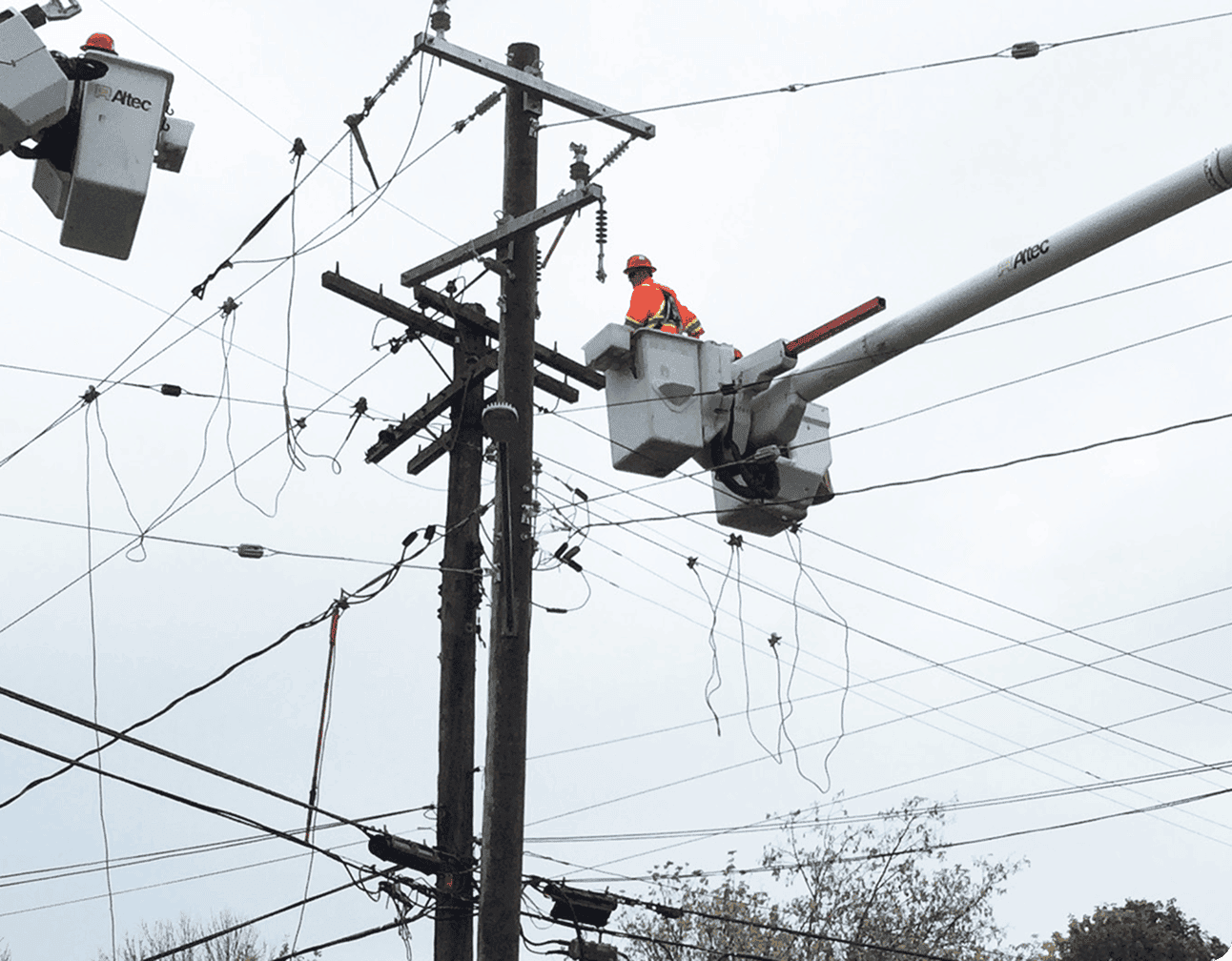 Bucket-truck lineman in safety gear repairing three-phase and secondary overhead distribution lines on a wooden utility pole