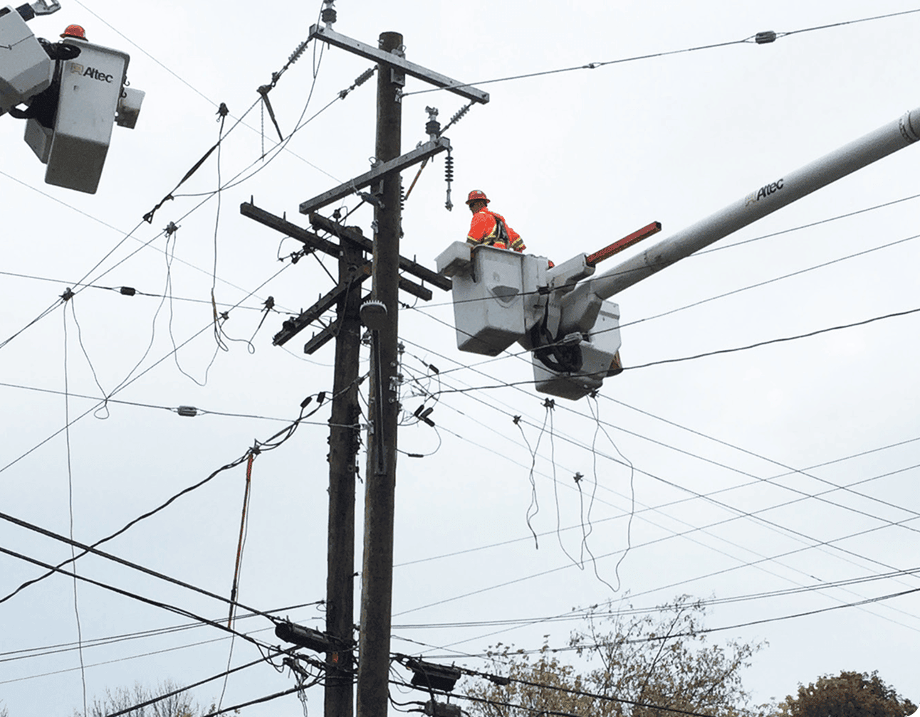 Lineman in orange safety gear in a bucket truck repairing tangled distribution wires on a wooden utility pole
