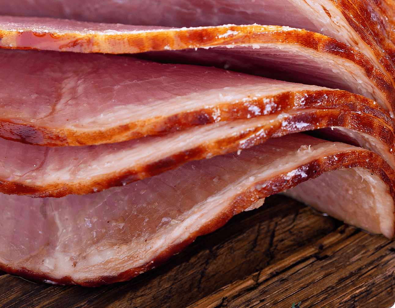 Close-up of glazed spiral-cut ham slices stacked on a wooden board, showing glazed edges and juicy pink meat texture