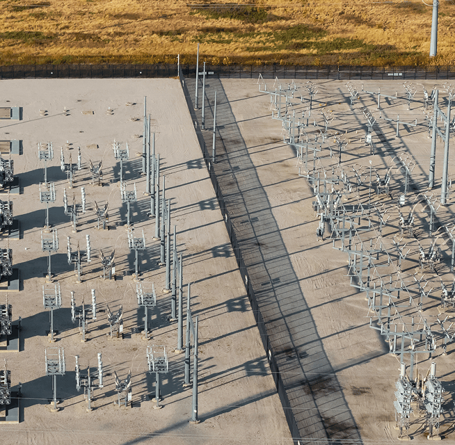 Aerial shot of electrical substation equipment with switchgear rows, transmission structures and fenced boundary