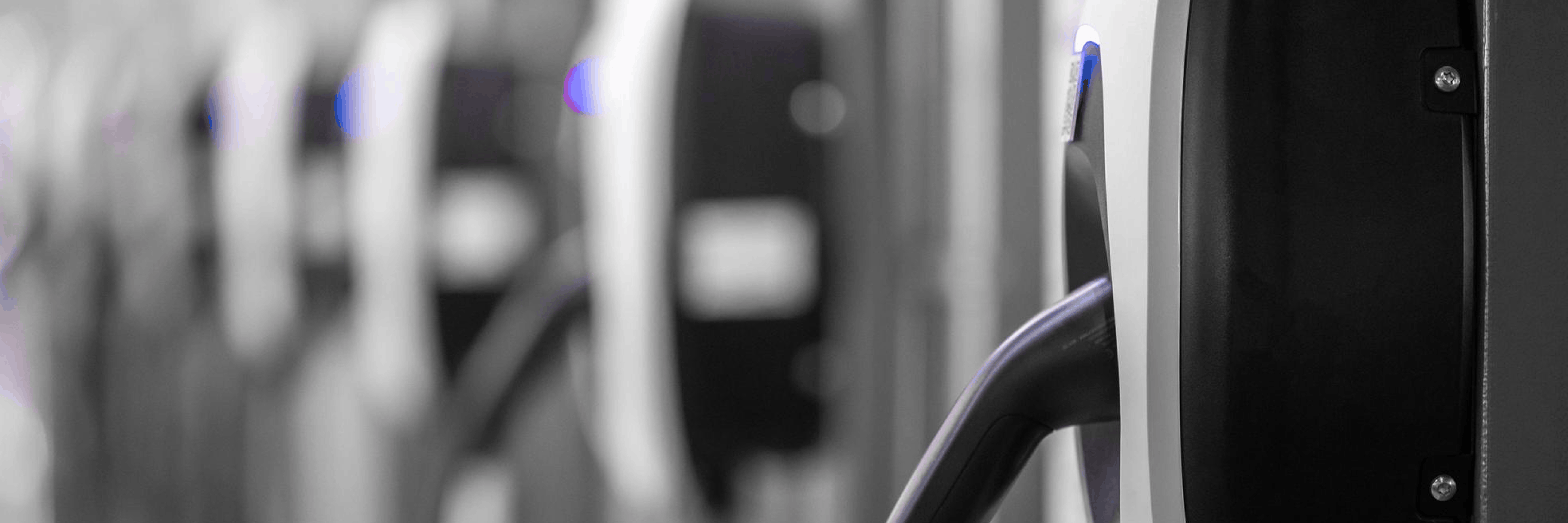 Close-up of an electric vehicle charging cable plugged into a wall-mounted EV charging station in a garage bay, grayscale