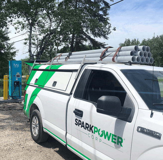 SparkPower service truck beside an EV charger, ladder rack loaded with PVC conduit and tools for installation