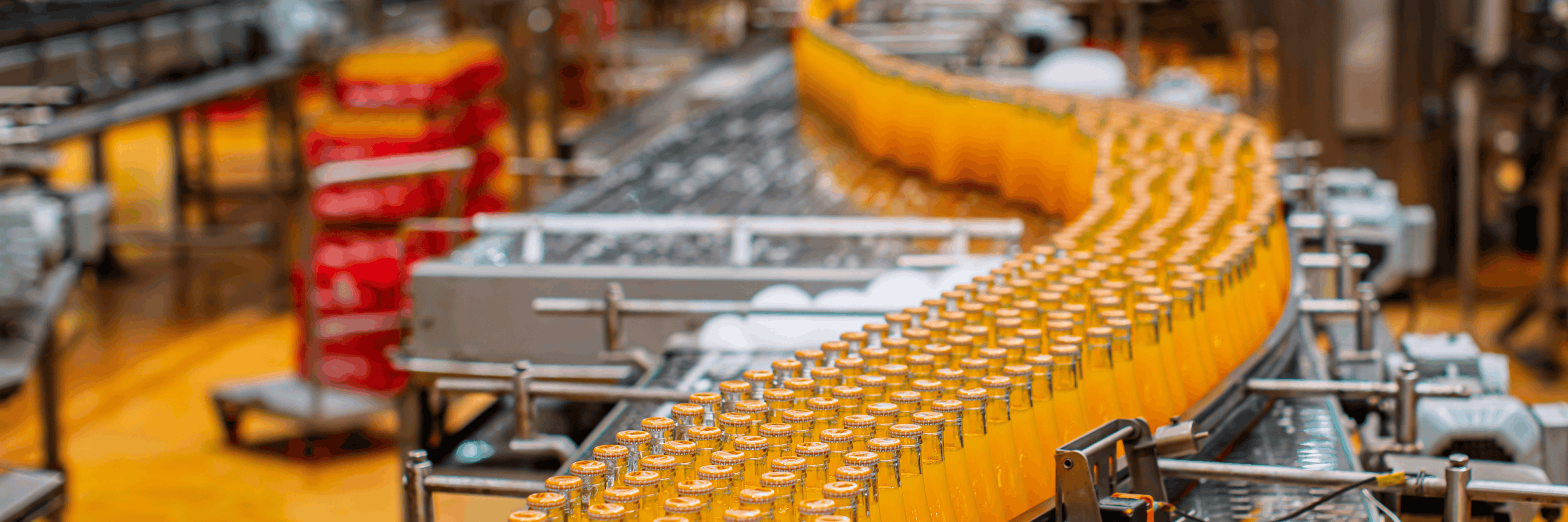 Bottled orange drinks on a curved stainless steel conveyor in a food and beverage plant with automated filling and capping
