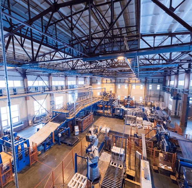 Industrial facility interior showing conveyors, robotic arms, blue steel framework and overhead trusses in a factory