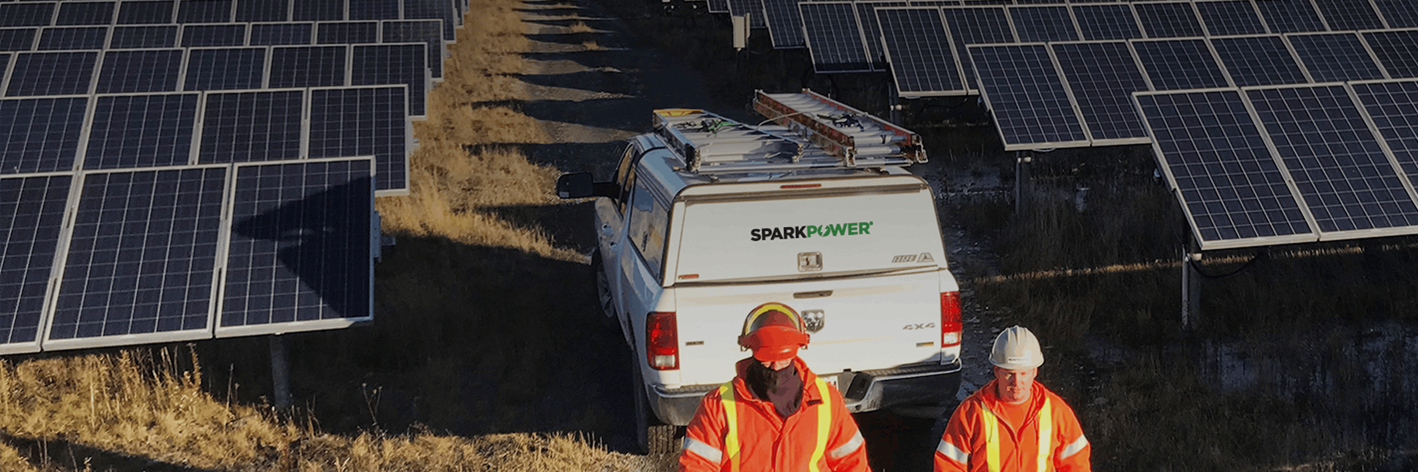 Two workers in orange safety gear beside a service truck among ground-mounted solar panels during maintenance