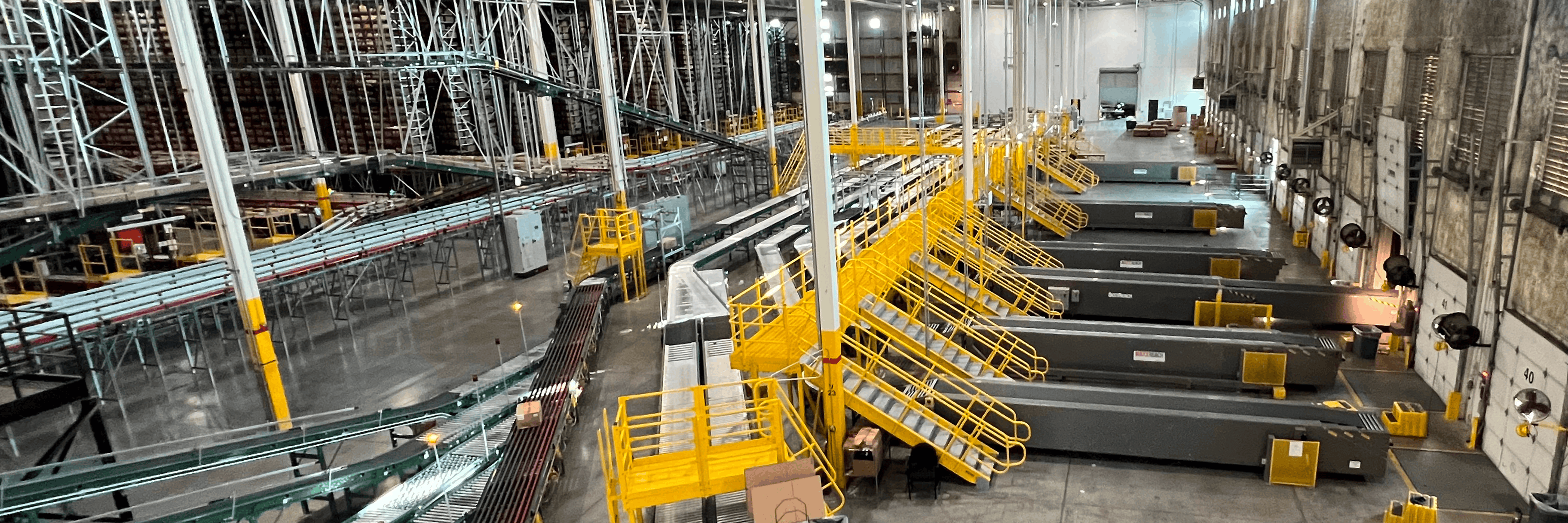 Wide warehouse interior showing conveyor lines, yellow access platforms, chutes and multiple loading docks for parcel sorting