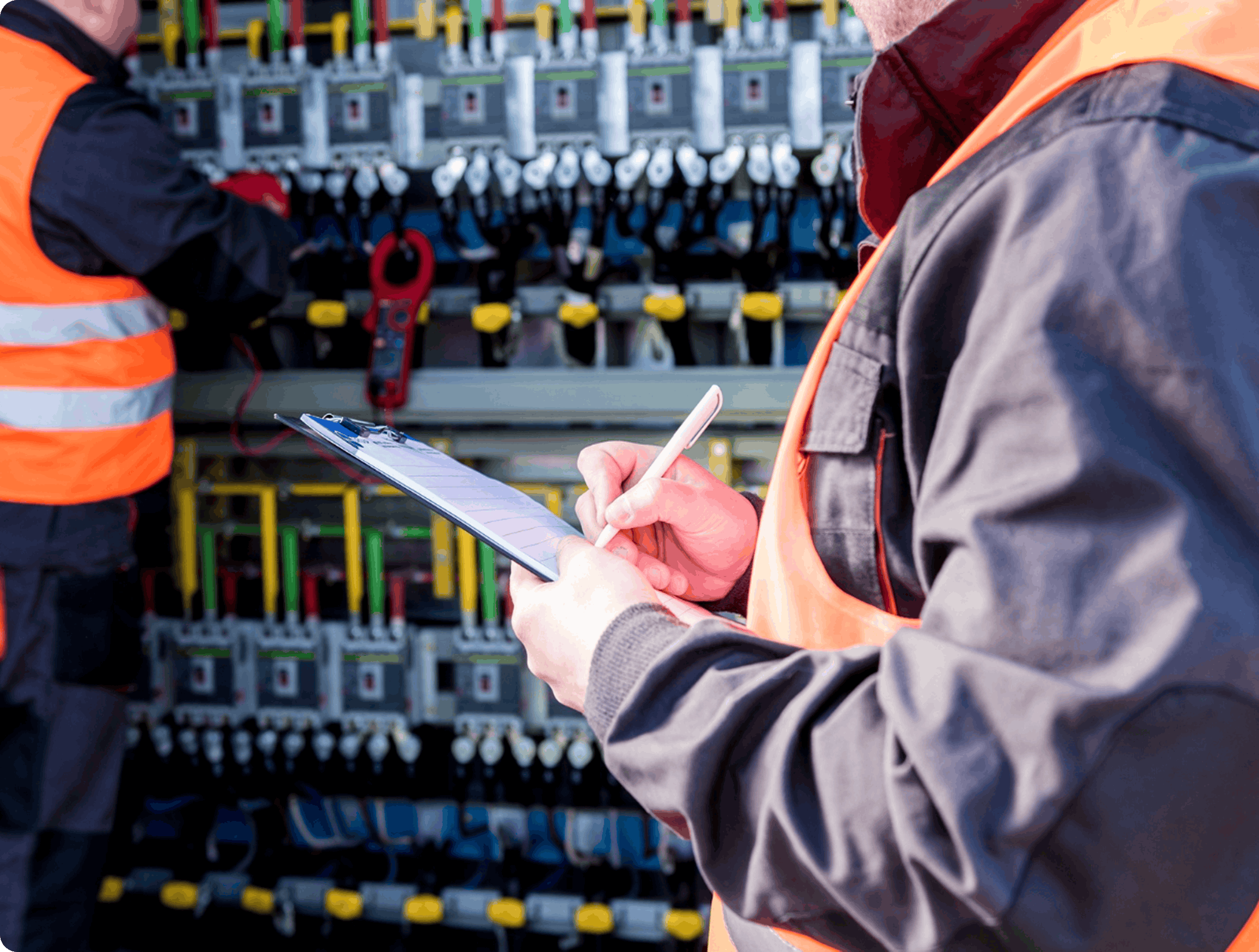 Technician in orange high-visibility vest inspecting electrical switchgear and recording readings on a clipboard
