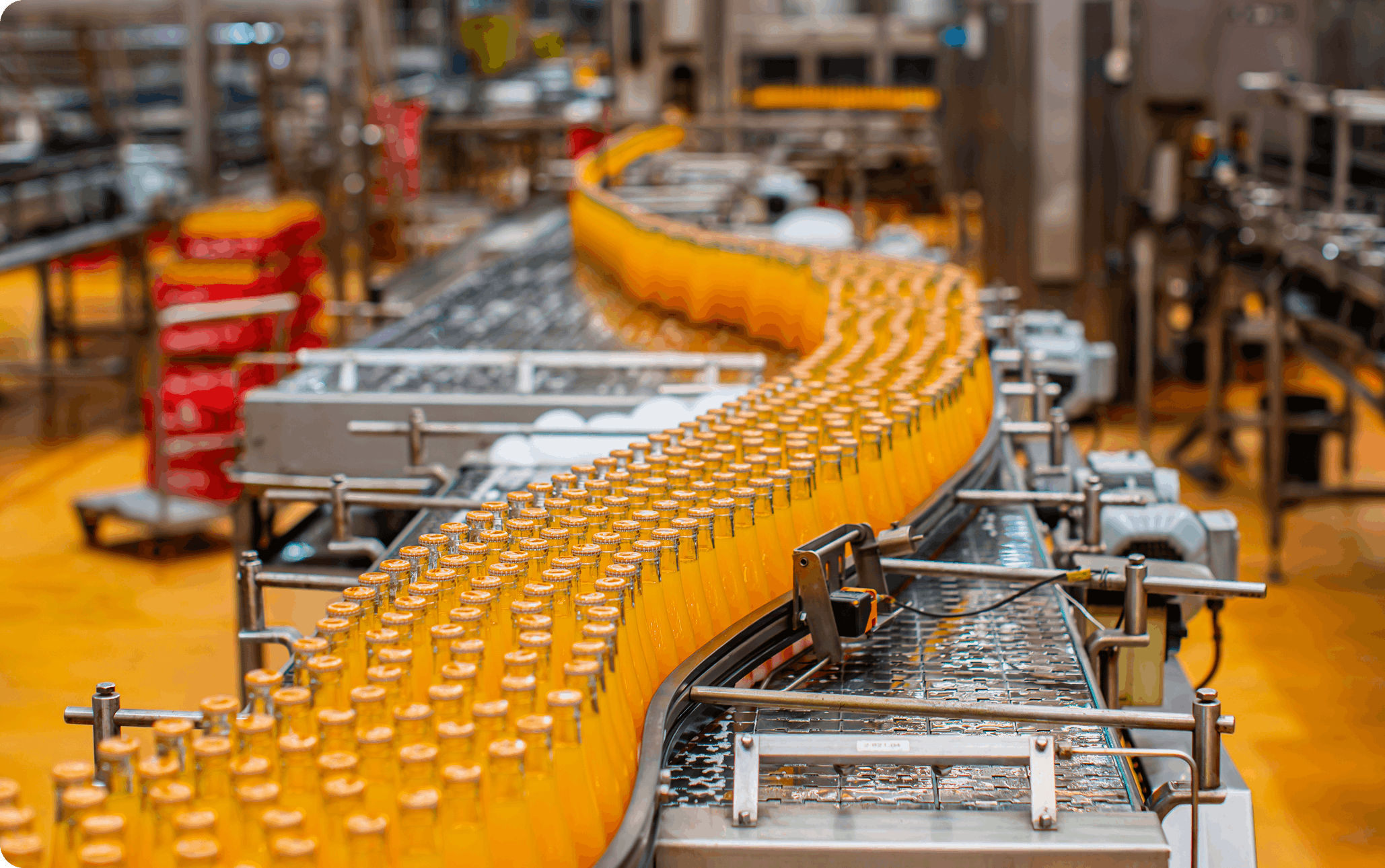 Row of orange-filled glass bottles on a curved conveyor inside a food and beverage production line with stainless equipment