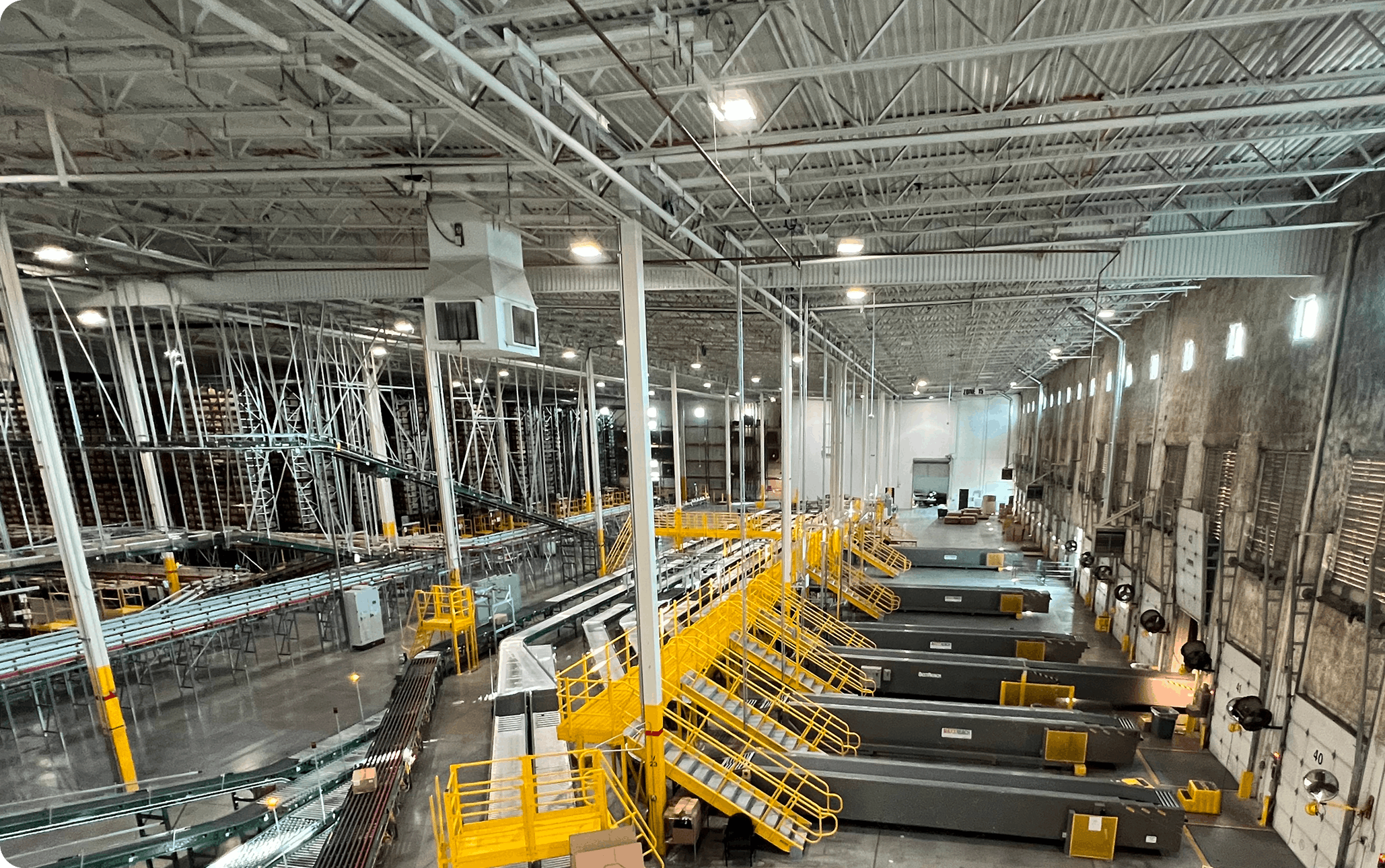 Distribution center interior showing yellow access walkways, multiple conveyor lines, chutes and high racking for sortation