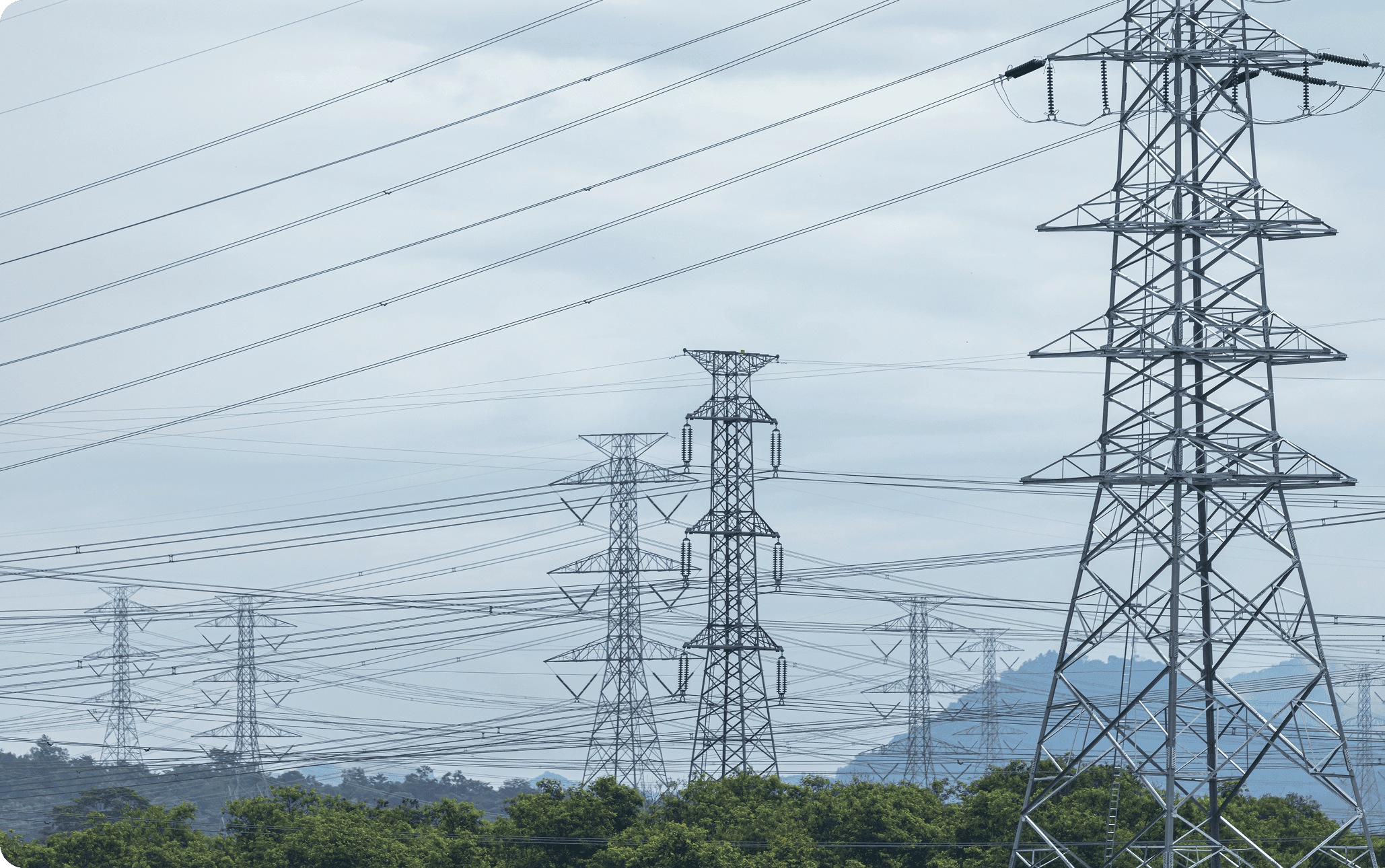 Steel high-voltage transmission towers and numerous overhead power lines crossing a misty landscape with trees