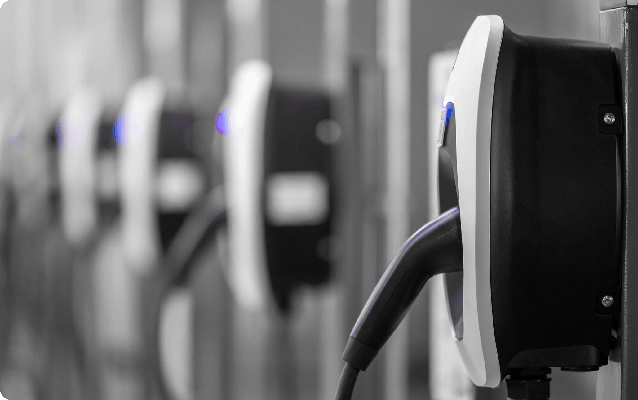 Row of wall-mounted EV charging stations with plugged Type 2 connectors in a commercial charging bay, focus on nearest unit