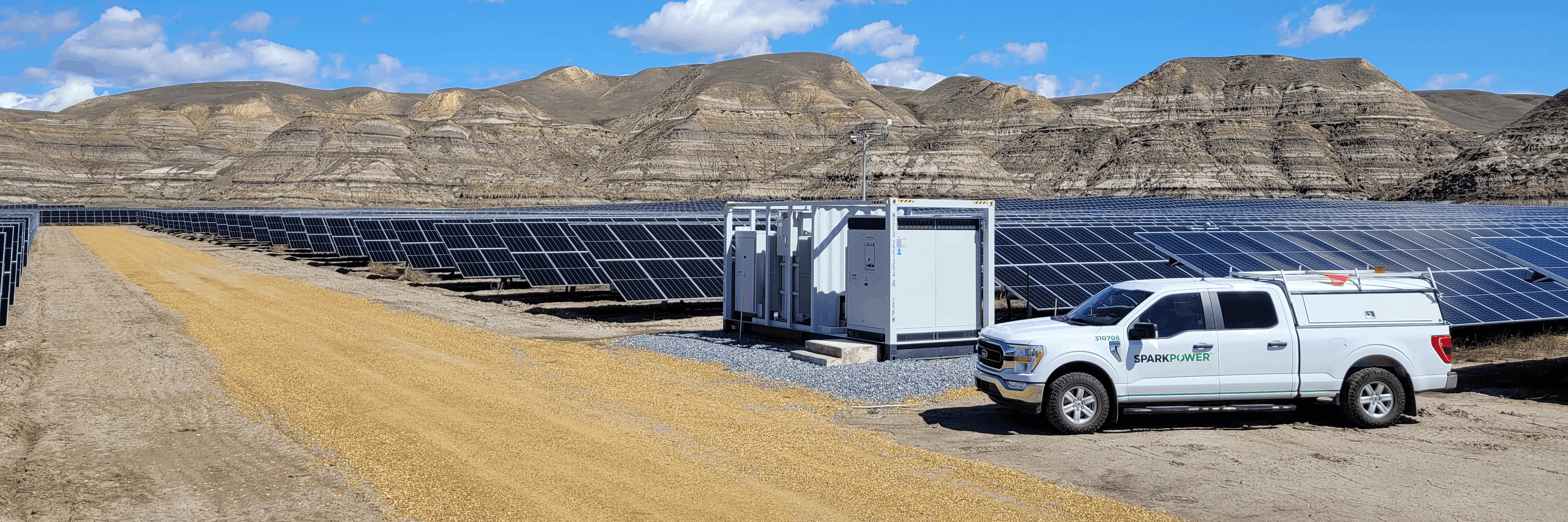 SparkPower truck next to electrical inverters and rows of ground-mounted solar panels at a large solar farm in arid terrain