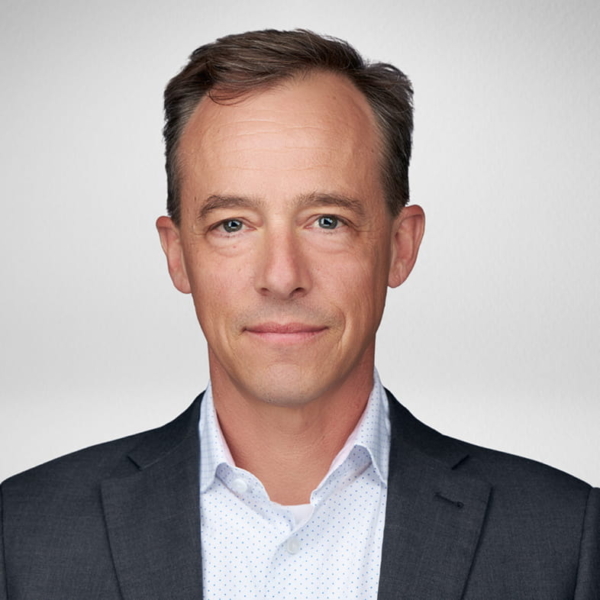 Male professional headshot of a suit-wearing company executive against a neutral gray studio background, facing camera
