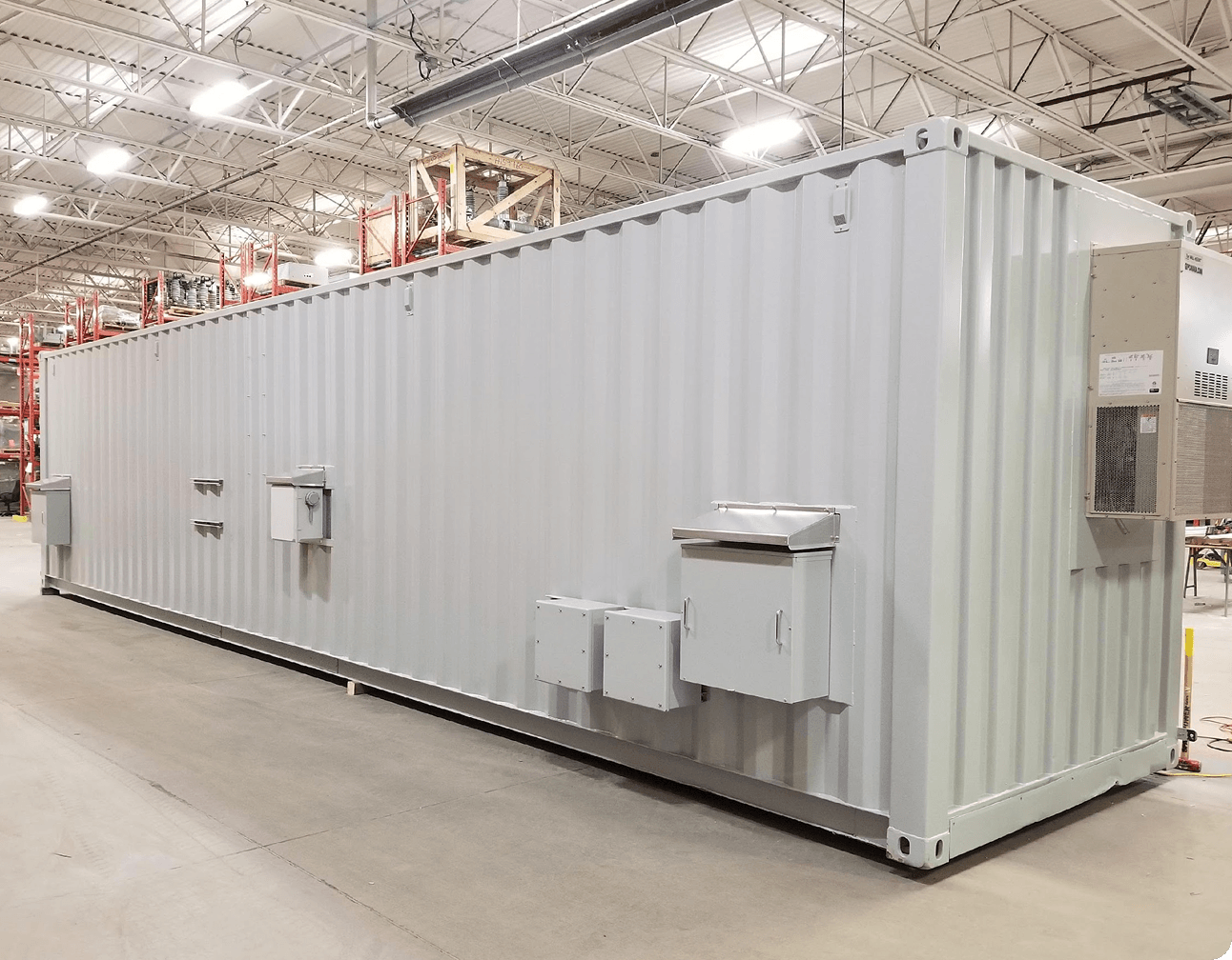 White modular electrical e-house inside a warehouse with multiple exterior access panels, junction boxes and air conditioner