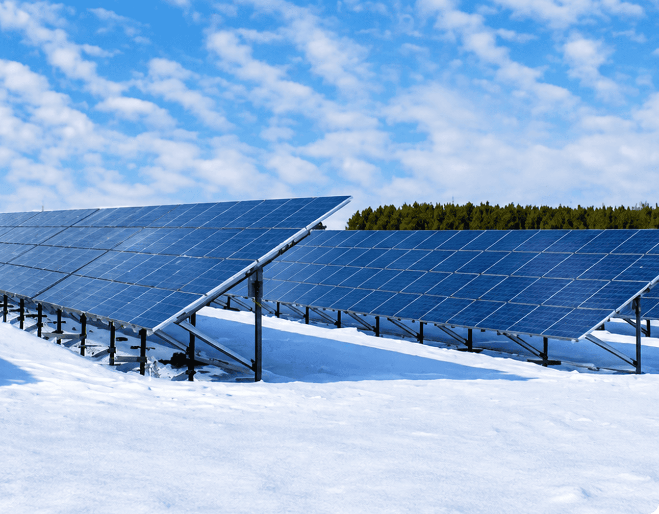 Ground-mounted solar panel arrays on metal racking installed in a snowy field under a blue sky for a renewable energy project
