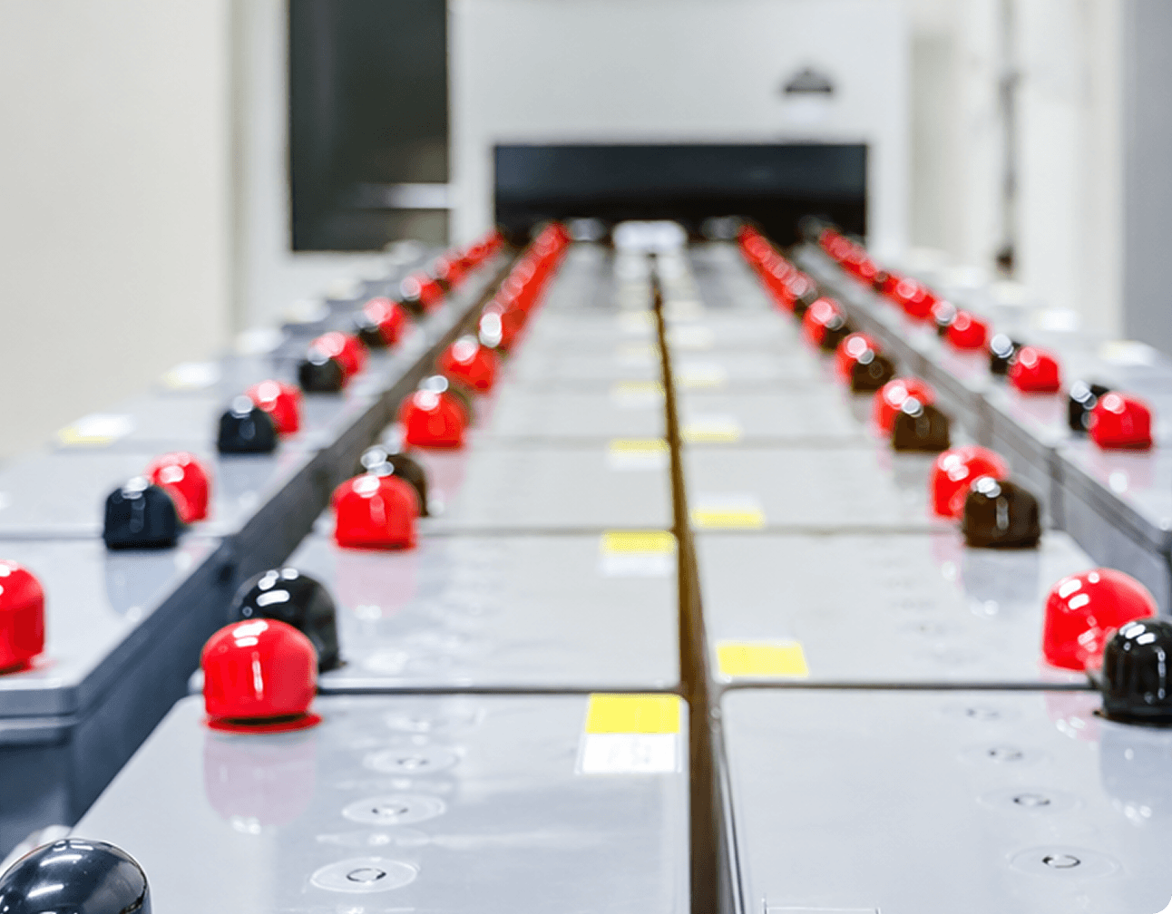 Rows of industrial battery modules with red and black terminal caps in a BESS electrical room supporting grid reliability