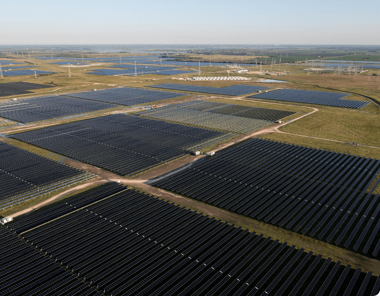 Aerial shot of a utility-scale solar array with dense PV panel rows, service roads and substation equipment visible