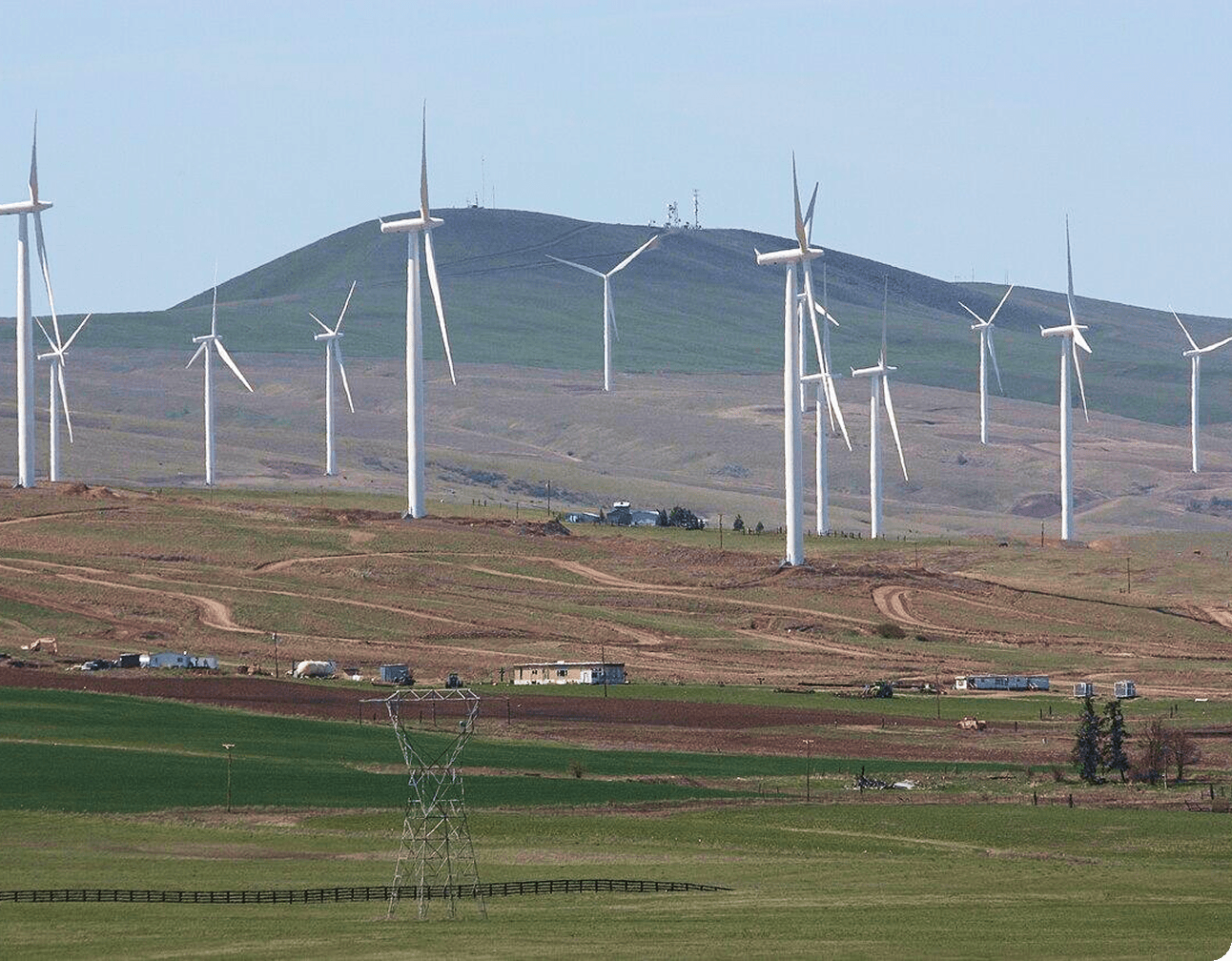 Utility-scale wind turbines across rolling hills with a distribution transmission tower in the foreground