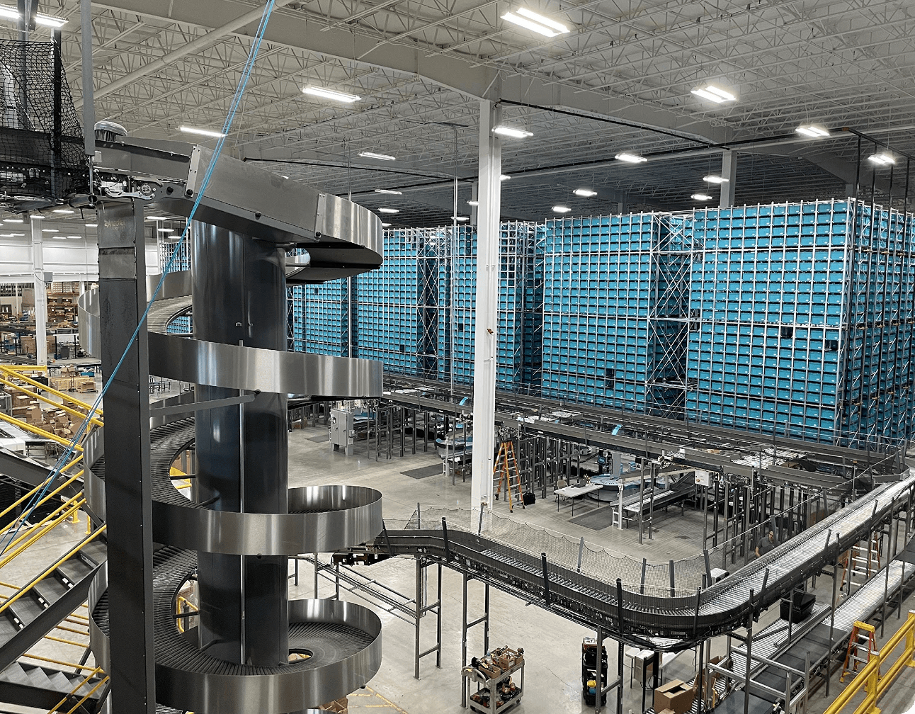 Spiral metal conveyor chute with conveyors and tall stacked blue storage bin racks in an automotive distribution facility