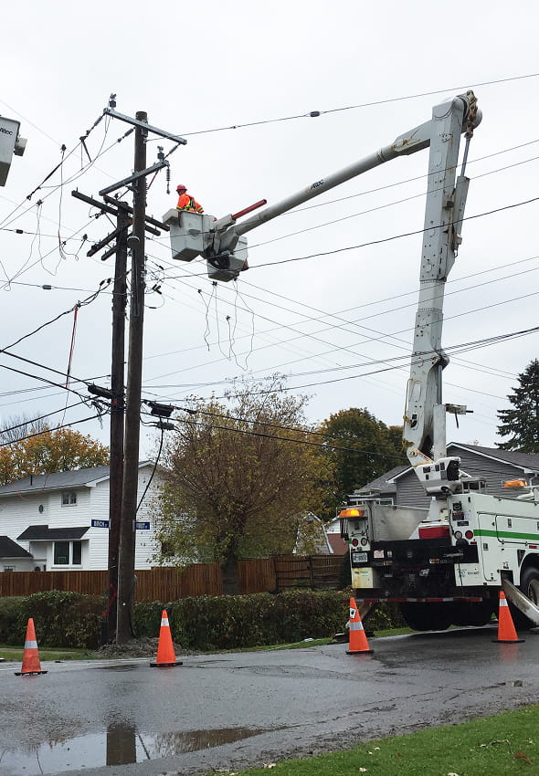 Bucket truck crew performing energized distribution line emergency repairs at a residential pole with traffic cones