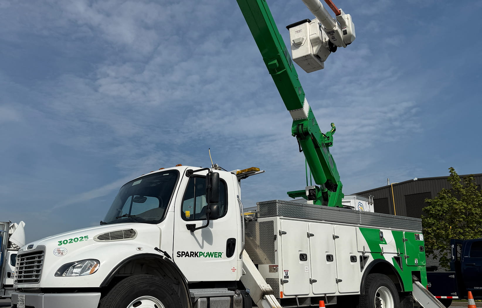 White SparkPower bucket truck with green articulated boom extended and utility service compartments under a blue sky