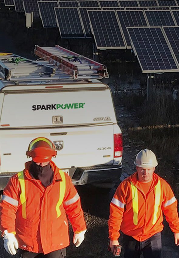 Spark Power technicians in orange high-visibility gear and hard hats beside a service truck at a solar panel maintenance site