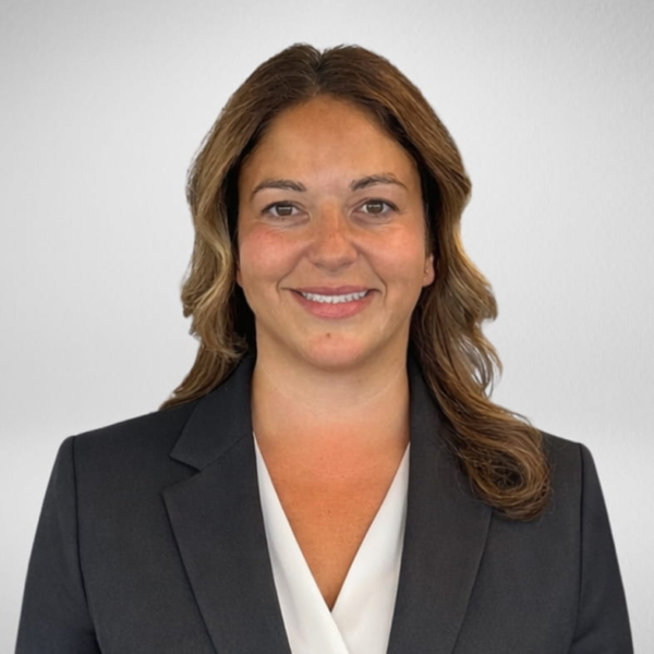 Female professional headshot with shoulder-length wavy hair, dark blazer and white blouse on gray backdrop